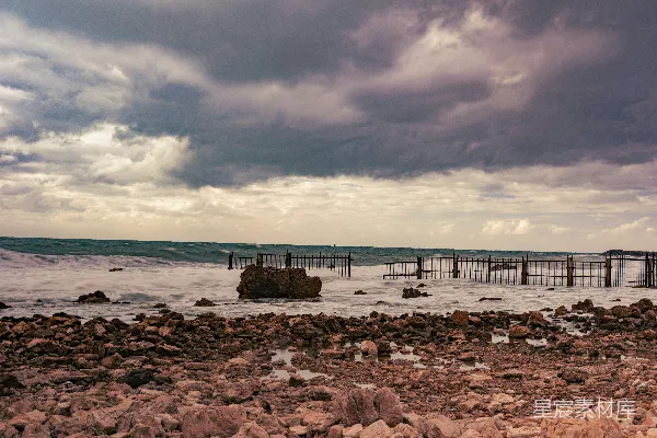 高清摄影 海滩上的人们站在傍晚的云层笼罩下的天空下 daytime, people stand on the beach shore under a cloudy sky.