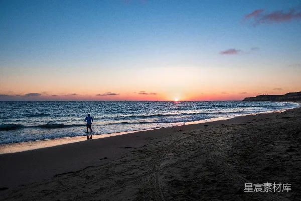 高清摄影 黑衣男子在海滩上夕阳西下时漫步。