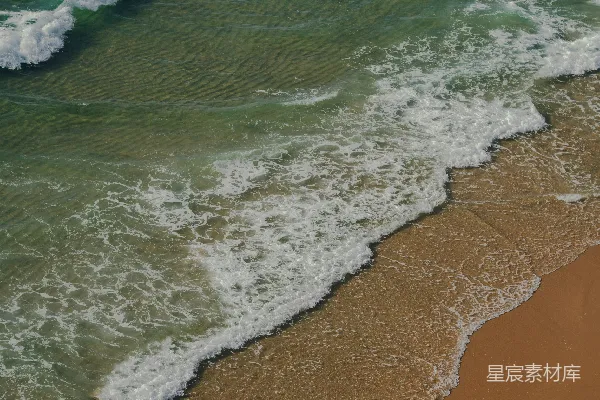 高清摄影 海边的一片沙滩，旁边是波涛汹涌的海洋。