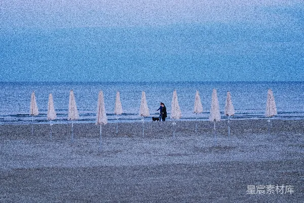 高清摄影 一个人在海滩上牵着一只狗走，有遮阳伞。