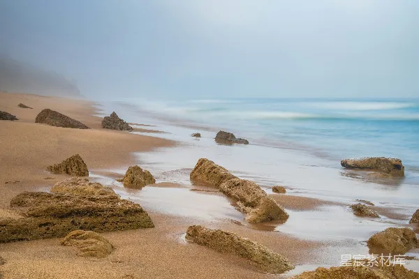 高清摄影 一片迷雾中的海滩场景，岩石与轻柔的波浪。