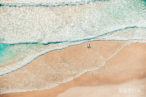 高清摄影 两个人在沙滩上行走，海浪拍打着岸边。