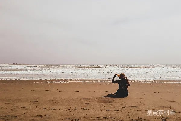 高清摄影 一位妇女坐在海滩上望着大海。