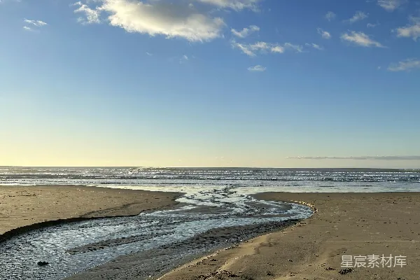 高清摄影 海边一片沙滩，靠近大海，蓝天白云下