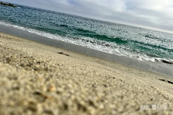 高清摄影 海边一片沙滩，靠近大海，天空阴沉。