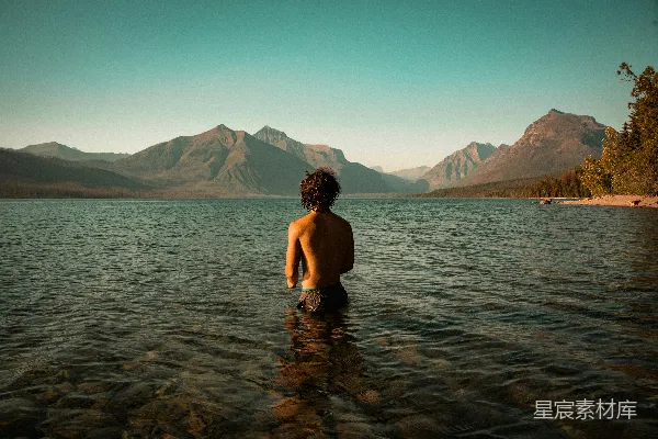 高清摄影 一个人站在水边，背景是山脉。