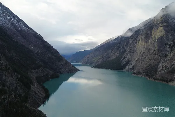 高清摄影 云层下，位于陡峭岩石山脉之间的蓝绿湖泊