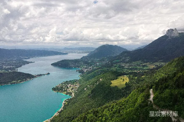 高清摄影 山脚下绿色的草地旁边有一片水域，白云下白天景色如画