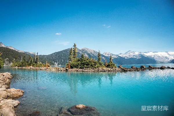 高清摄影 vibrant turquoise lake, forested islands, and snowy mountains.