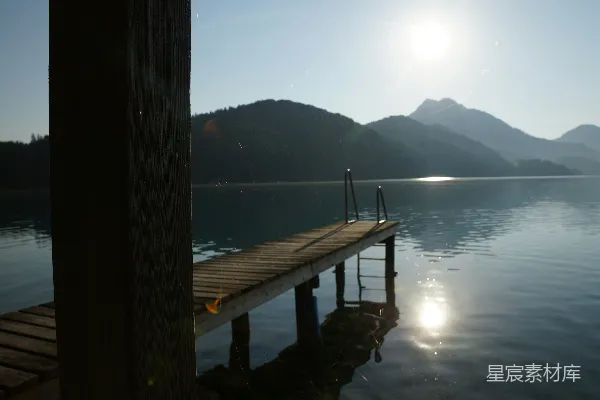 高清摄影 木制栈桥置于宁静湖泊畔，日出时分山峦在侧。