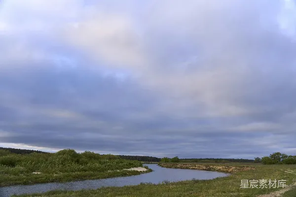高清摄影 蜿蜒的河流穿过一片草地，在云层下流淌。