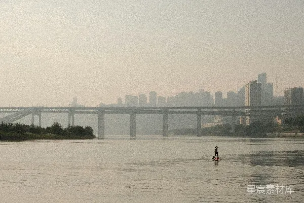 高清摄影 河边一条独木舟上独自划桨者，背景是城市 skyline。