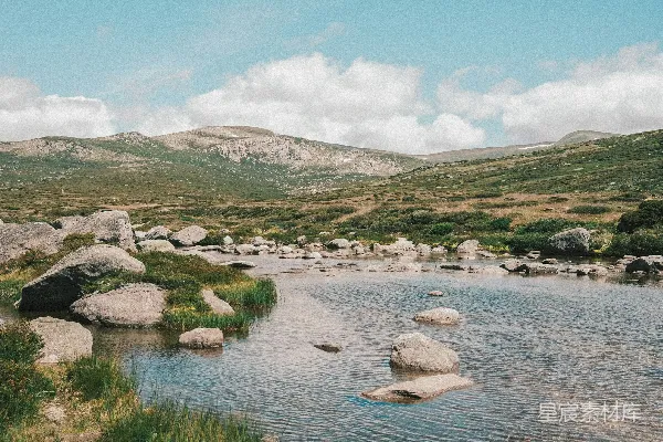 高清摄影 一条河流被岩石和草包围，背景是山脉。