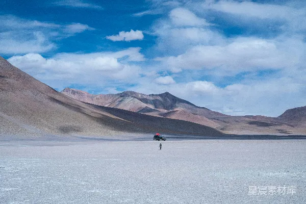 高清摄影 一个人走在沙漠平原上，背景是山峦。
