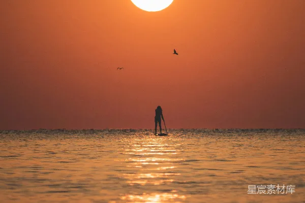 高清摄影 夕阳下的海边，一个人站在冲浪板上。