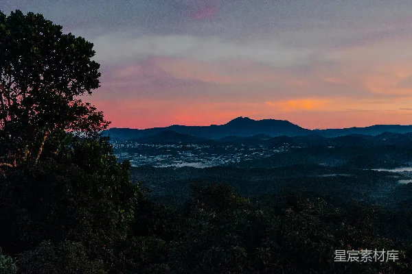 高清摄影 山脚下一片山峦的夕阳美景，前景中有一棵树。