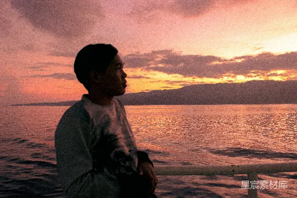 高清摄影 穿着灰色毛衣的男人坐在海滩上，夕阳西下时。