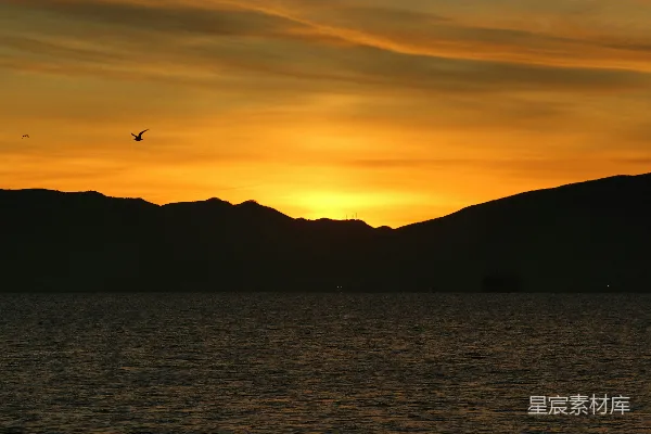 高清摄影 夕阳映照在一片水体上，山峦在背景中若隐若现。