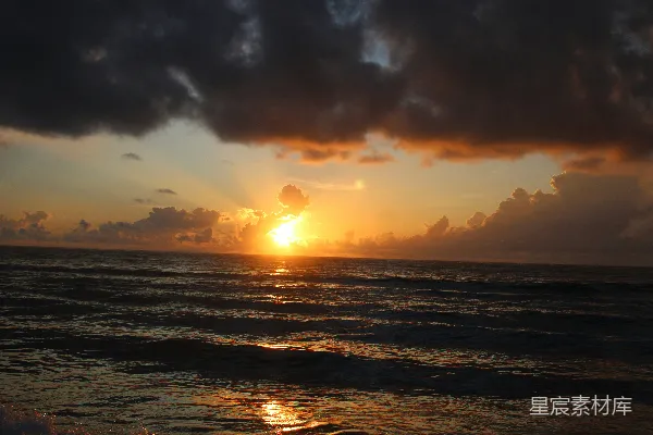 高清摄影 在一片乌云密布的天空下，夕阳正沉落在海面上。