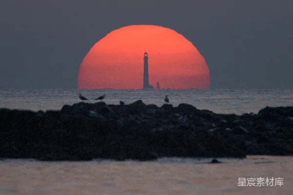 高清摄影 夕阳下橙色球体靠近黑色岩石附近，周围环绕着水面。