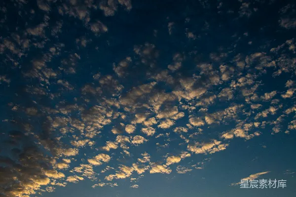 高清摄影 夕阳映衬着天空中散落的云朵，背景为深蓝色。