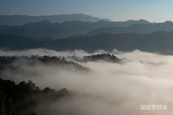 高清摄影 云雾缭绕的山脉，树木环绕，远处耸立着塔楼。