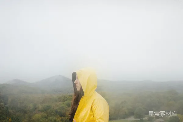 高清摄影 一个穿黄雨衣的女人站在山顶上。