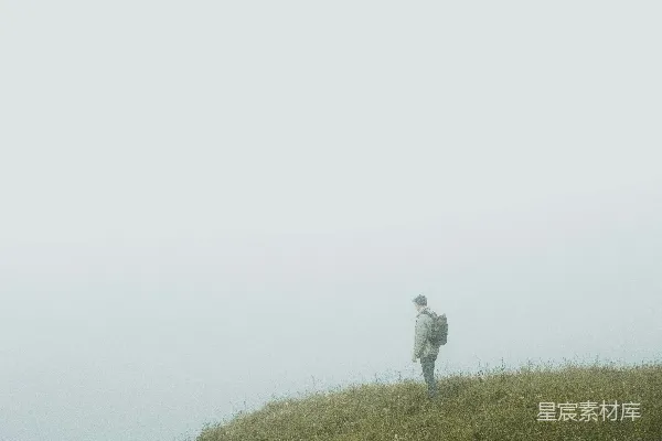 高清摄影 白色上衣的人在绿草地上方的雾天里站立。