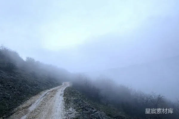 高清摄影 一条尘土路蜿蜒穿过一片雾气缭绕的山地景观。