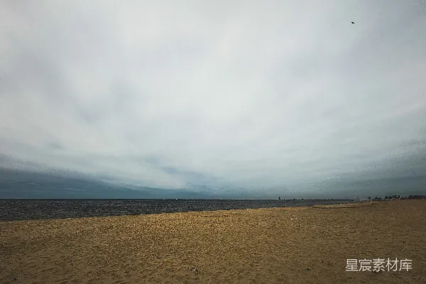 高清摄影 沙滩上撒满细沙，云层遮蔽的天空下是大海。
