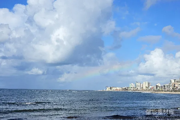 高清摄影 远处彩虹映衬下的海浪和城市天际线。