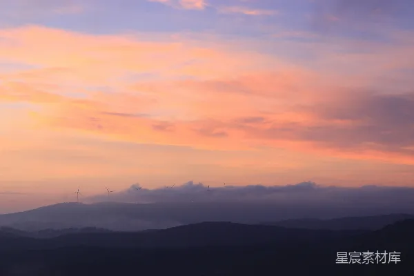 高清摄影 夕阳下，淡粉色的云层覆盖在深色山峦之间。