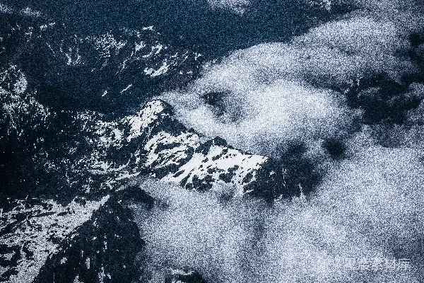 高清摄影 白天的高空照片中，白雪覆盖的灰色山峰上方飘着白云。