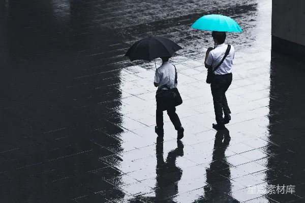 高清摄影 两人在雨中行走于路旁，撑着伞。