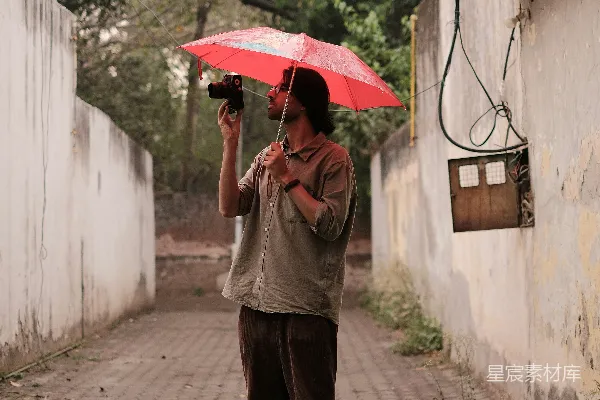 高清摄影 一个男子手持红色雨伞站在砖石路上。