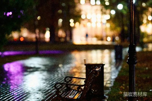 高清摄影 夜晚公园长椅上坐着一个人，旁边是湿漉漉的 sidewalk 。