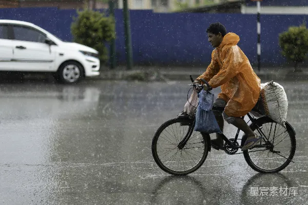 高清摄影 身穿橙色雨衣的人骑自行车穿过大雨。