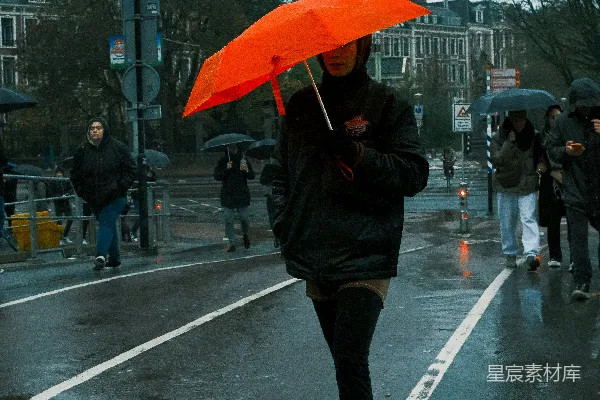 高清摄影 手持橙色伞的人在雨中行走。