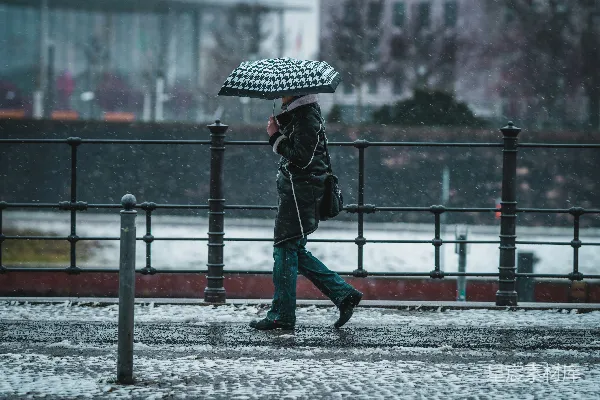 高清摄影 黑色夹克和蓝色牛仔裤的人手持雨伞在覆盖着白雪的道路中行走。