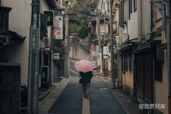 高清摄影 身穿粉红色雨伞的人走在狭窄的街道上。