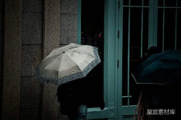 高清摄影 夜晚行人手持雨伞走过一栋建筑旁。