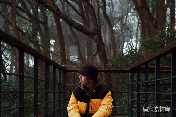 高清摄影 穿黑黄夹克的男人坐在树旁。