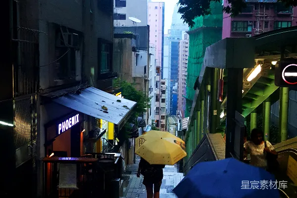 高清摄影 街道两栋建筑之间的人们手持蓝色和黄色的伞