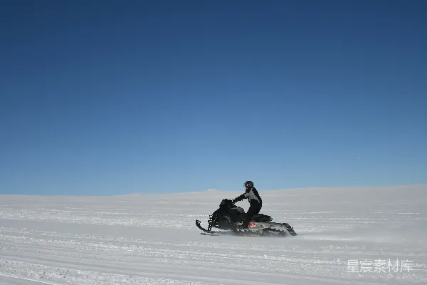 高清摄影 人在雪地平原上驾驶雪地摩托，天空晴朗蔚蓝