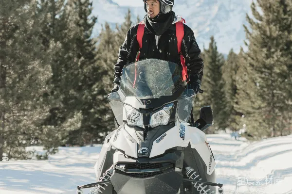 高清摄影 黑色风衣的男人驾驶着白色的雪地摩托在覆盖着积雪的地面上白天行驶。
