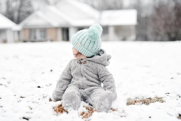 高清摄影 灰衣儿童穿着绿色针织帽坐在覆盖着积雪的地面上的白天场景