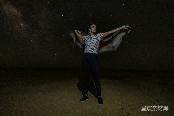 高清摄影 一个男人站在一片沙漠的中央，在满天闪烁着星星的夜空下。
