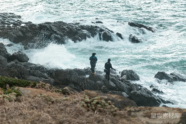 高清摄影 黑色夹克的男人站在海边岩石上，白天靠近海浪。