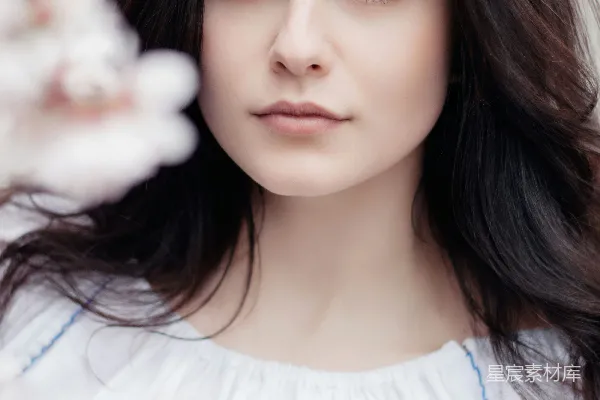 高清摄影 女人站在一旁，近处站着一朵有白色花瓣的花。