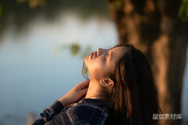 高清摄影 一个女人站在树旁闭着眼睛。